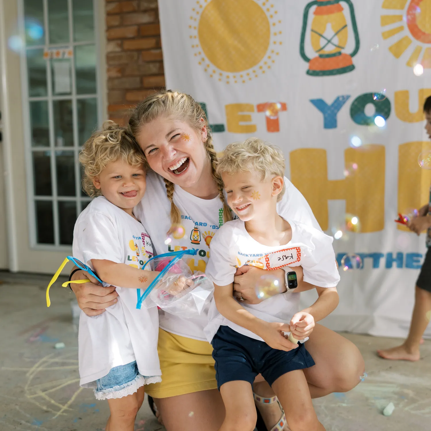 A Backyard VBS host laughing with two neighborhood kids after a day outdoors
